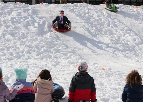 Students watching as a student on a sled slides down a hill of snow